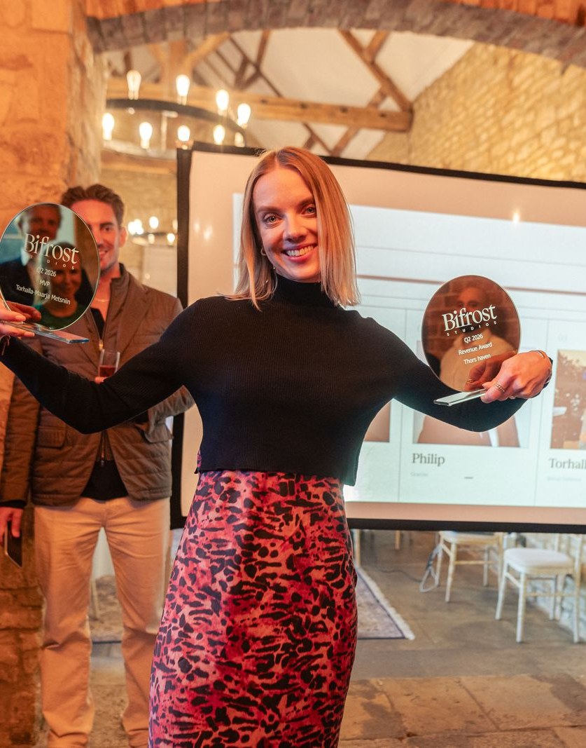 A colleague holding up two Bifrost Studios awards in a stone-vaulted barn, the room applauding