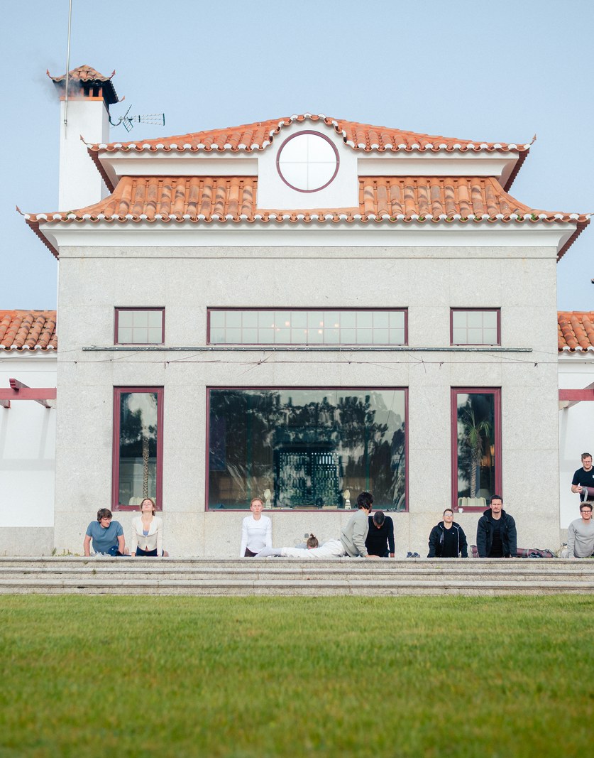 A white villa with a tiled roof, the team sitting on its steps in the morning light