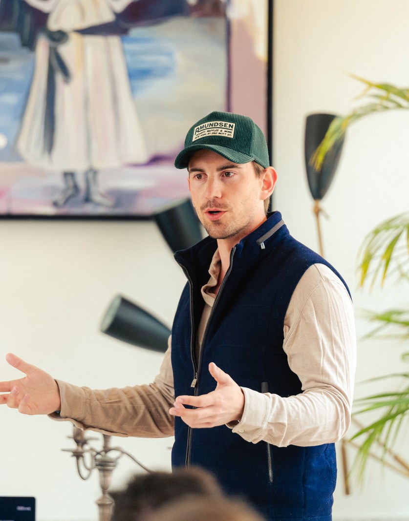 A speaker in a cap talking to the room, a Bifrost banner beside him