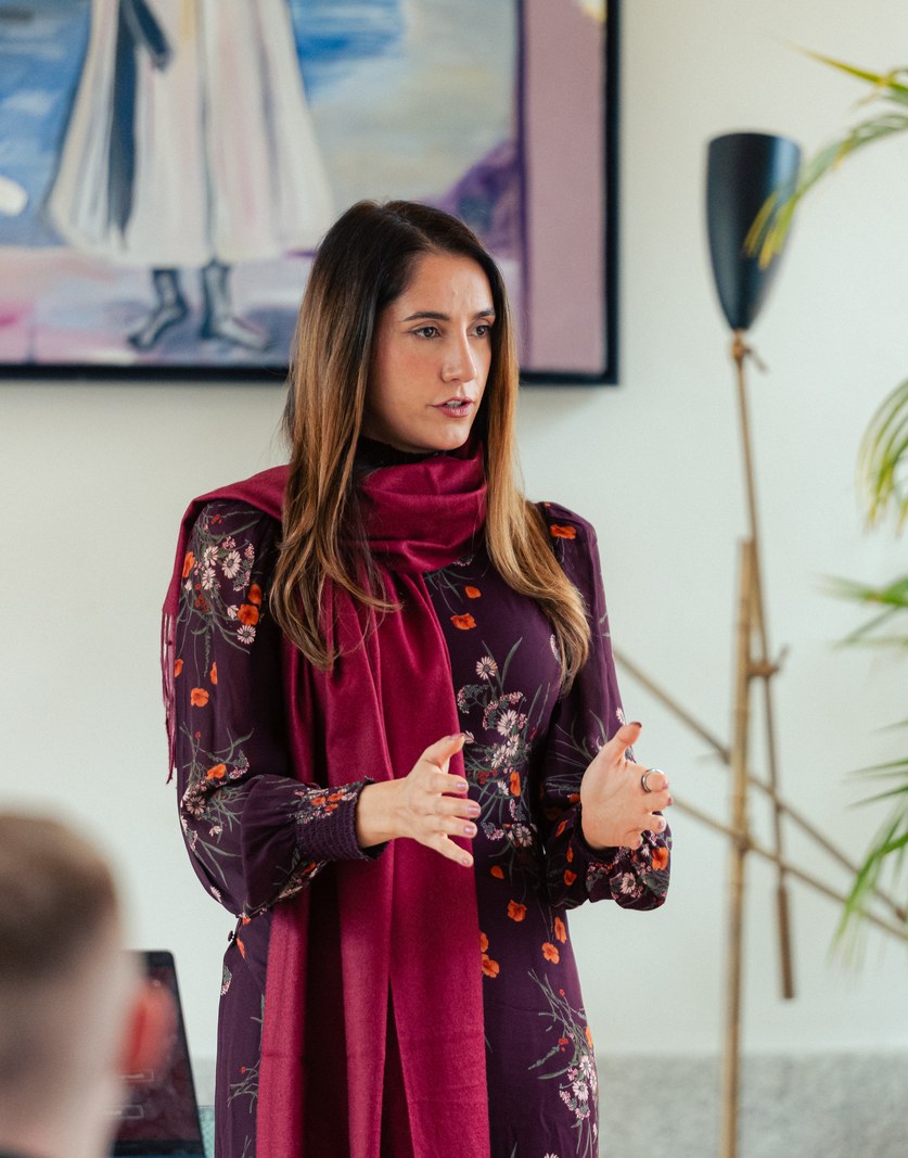 A speaker in a burgundy dress making a point to a room of laptops